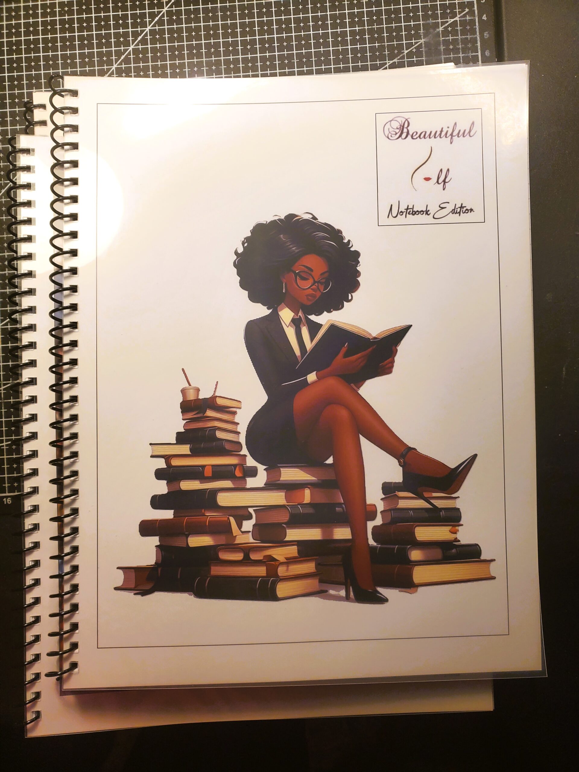 Spiral Note book with an image of a woman reading and sitting on a stack of books